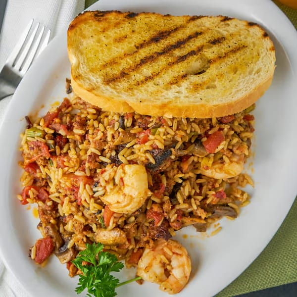 Southern jambalaya with shrimp, tomatoes, and rice, served with grilled toast on a white plate.