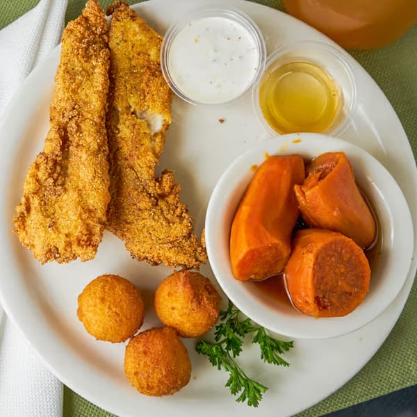 Southern fried catfish, hush puppies, and candied yams with dipping sauces on a white plate.