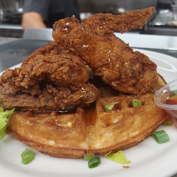 Crispy fried chicken pieces drizzled with syrup on a golden waffle, garnished with green onions.